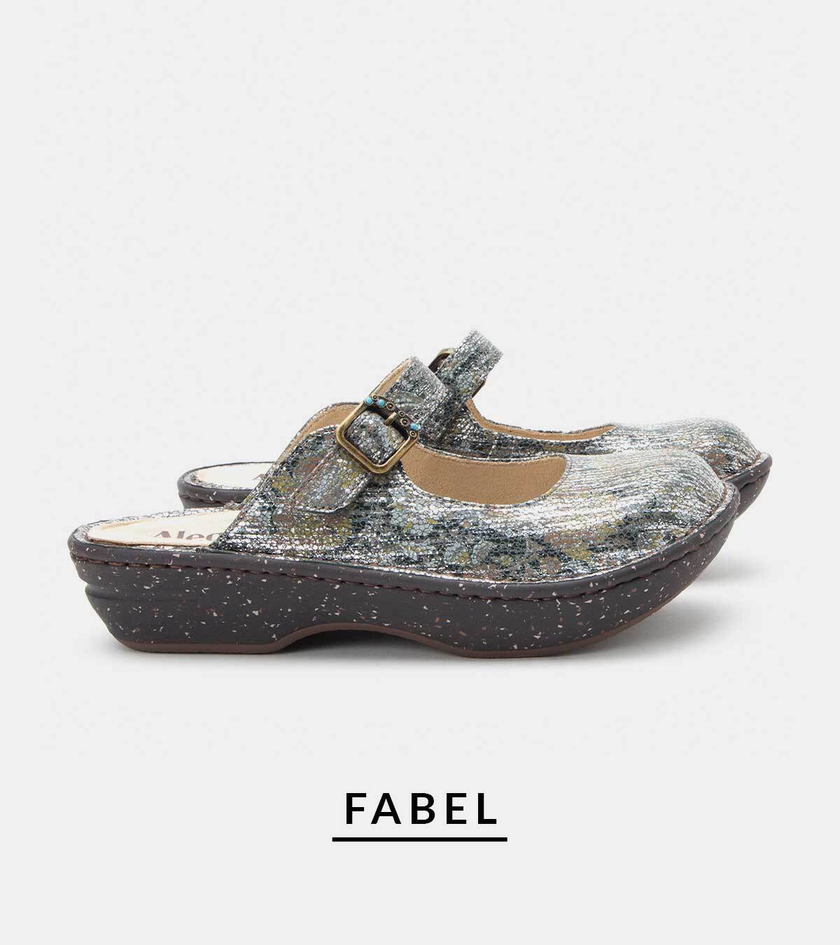 Pair of metallic silver textured mule clogs with an adjustable instep strap, antique gold buckle, and specked dark outsole. Product name "FABEL" displayed underneath on a light background.
