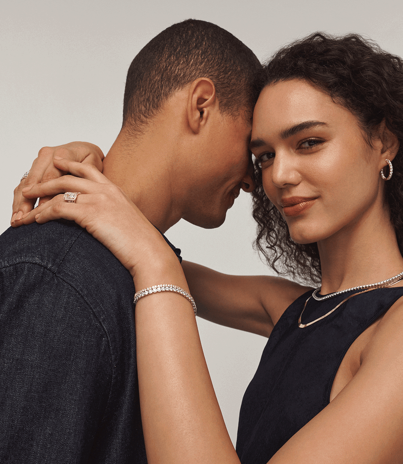 A model hugging another, wearing a rectangular diamond ring with matching diamond and gold jewellery.