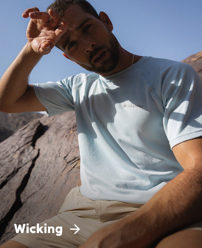 A man sitting on a rock wearing a short sleeve blue shirt with text: Wicking