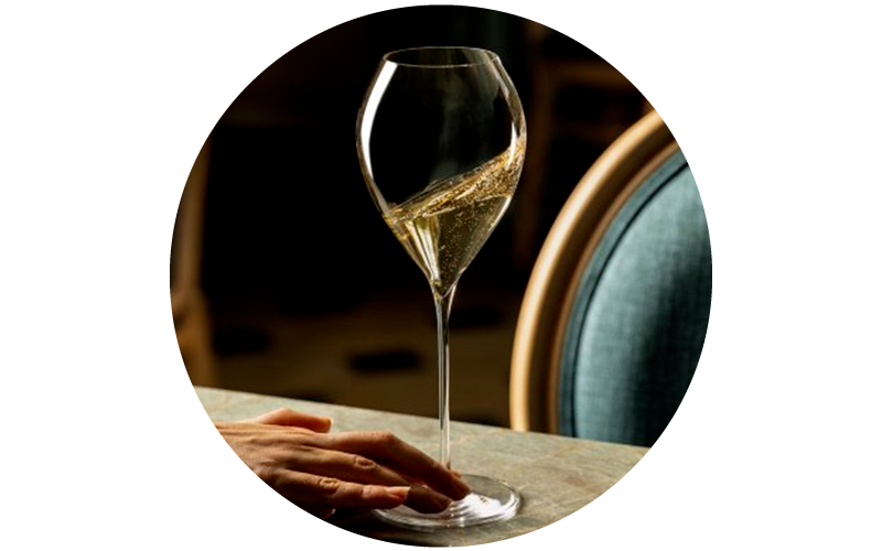 Long-stemmed wine glass of sparkling white wine with bubbles on a table beside a seated person's hand in an elegant restaurant