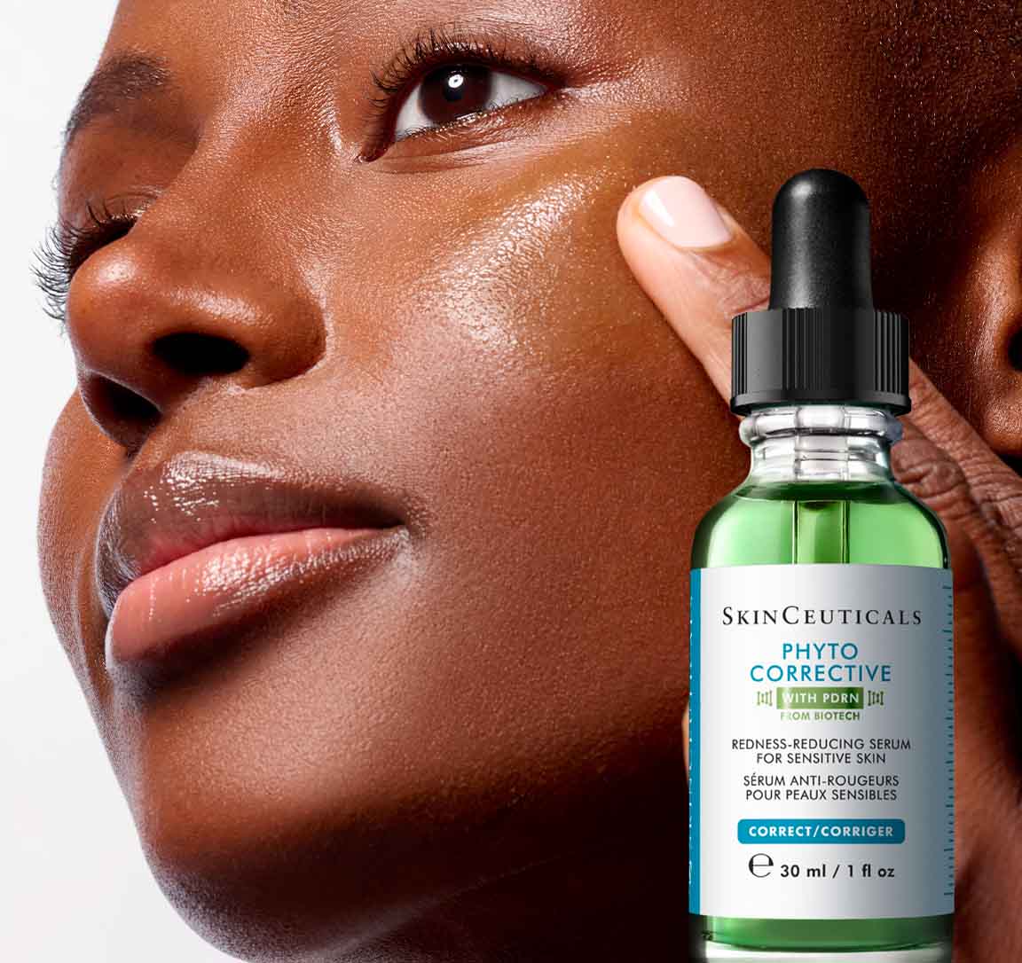Nahaufnahme eines Models mit strahlender Haut, das auf die Wange zeigt, neben einer Flasche des SkinCeuticals Phyto Corrective Serums vor hellem Hintergrund.