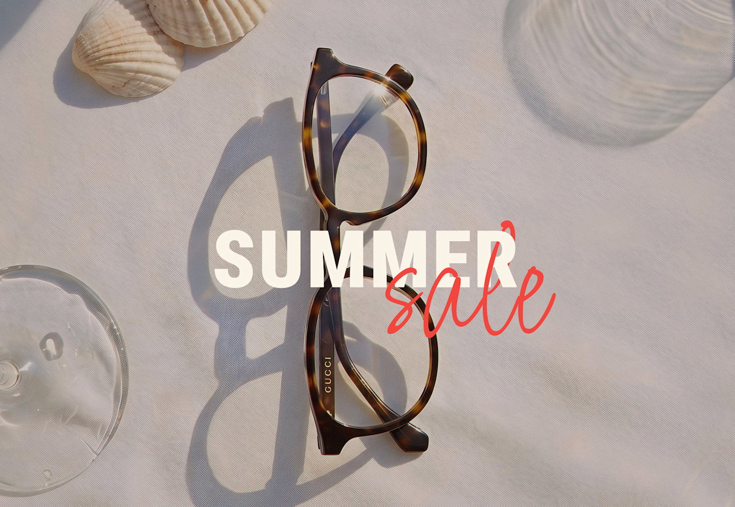 Brille auf hellem Leinenstoff, umgeben von Muscheln, "Summer Sale" in weiß und rot.