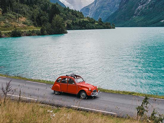 Eine rote Oldtimer Ente fährt am See entlang.