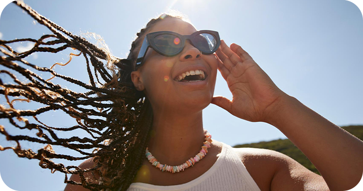 Lächelnde Frau mit Sonnenbrille im Freien bei sonnigem Wetter.