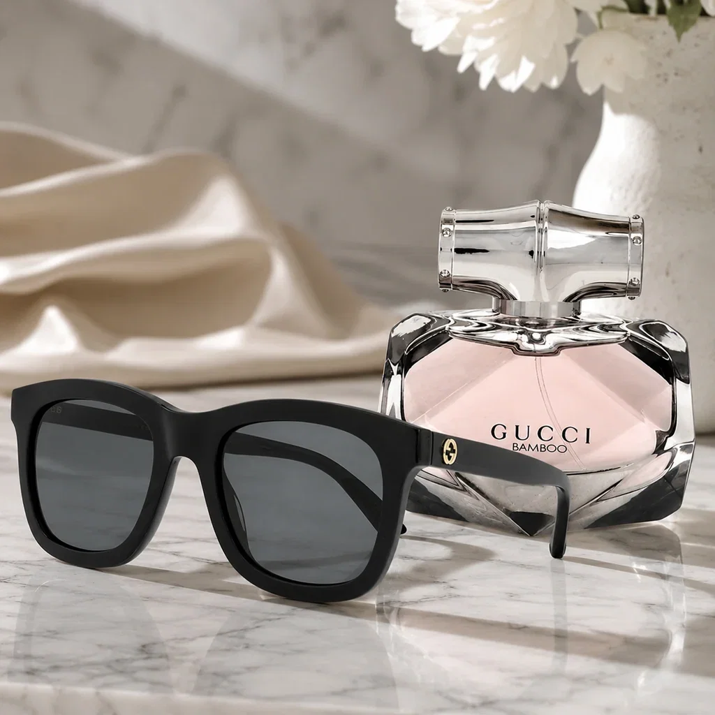 Gucci Bamboo perfume and black sunglasses displayed on marble surface with white flowers and cream tableware.