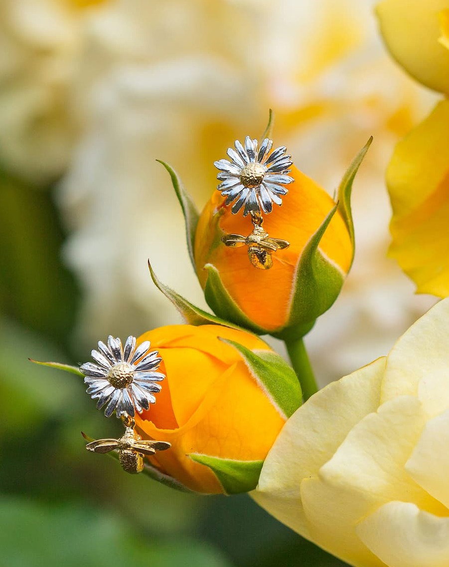 Alex Monroe Daisy Stud Earrings with Teeny Tiny Bee Drops displayed amongst vibrant orange and yellow flowers.