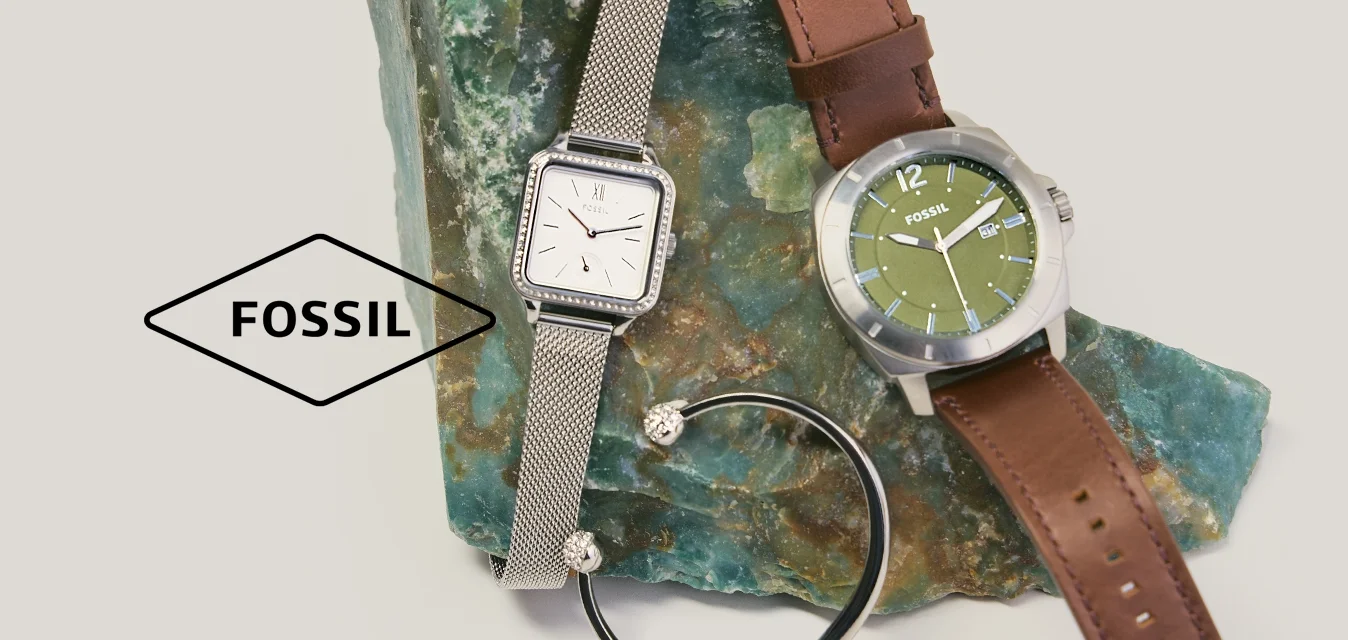Deux montres-bracelets — une argentée avec un bracelet en maille, une avec un cadran vert et un bracelet en cuir marron — et un bracelet noir sur une pierre verte rugueuse.