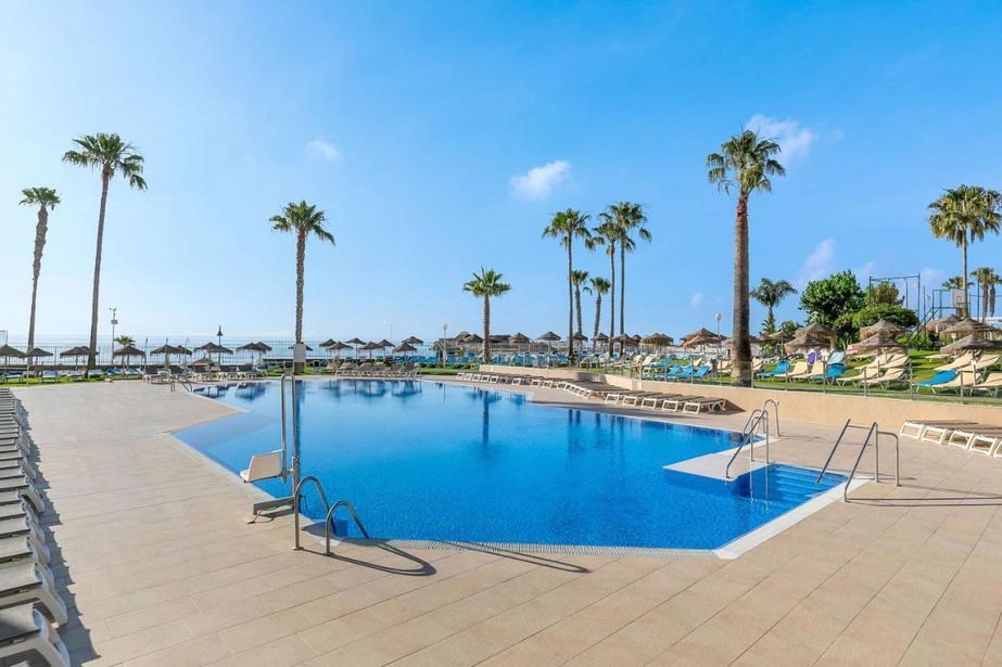 Resort outdoor swimming pool with sun loungers and palm trees overlooking the sea under a clear blue sky