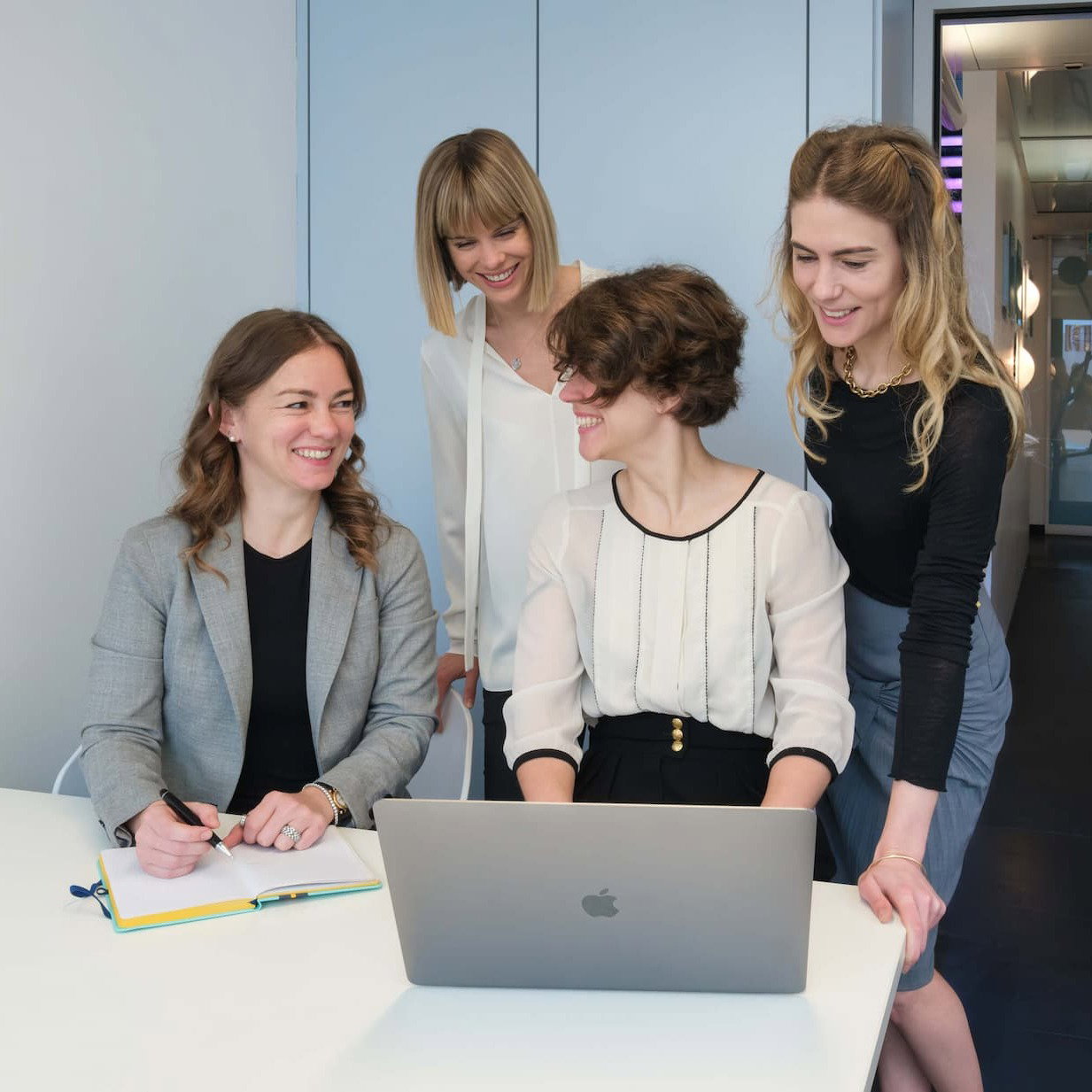 An image of the Polla Sisters sitting at a desk smiling at each other.