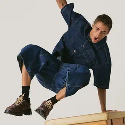 Man in spijkeroutfit springt over een houten turnbok met één hand die zijn val ondersteunt.