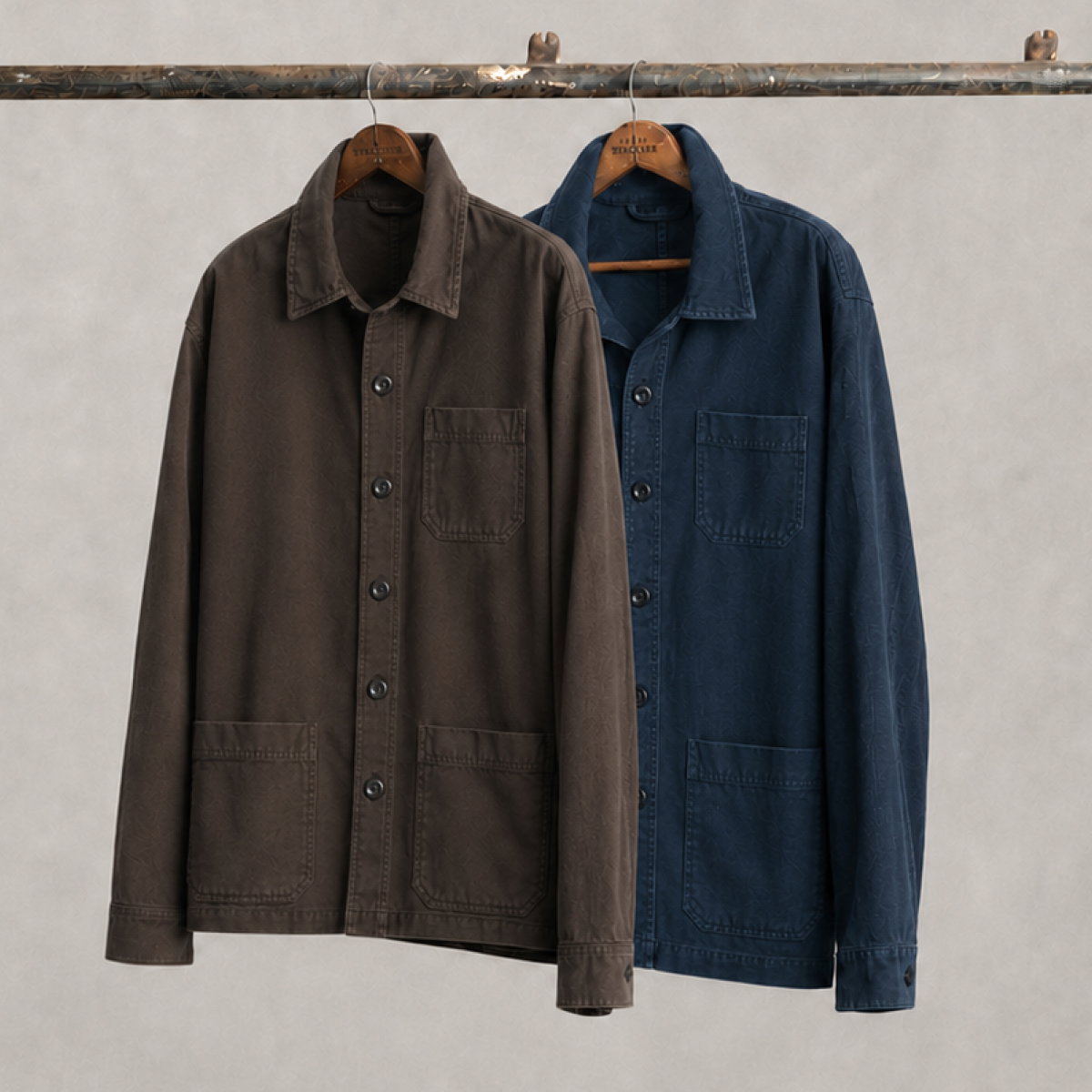 Two Bills Khakis Dune Twill chore jackets hang from hangars on a industrial pole