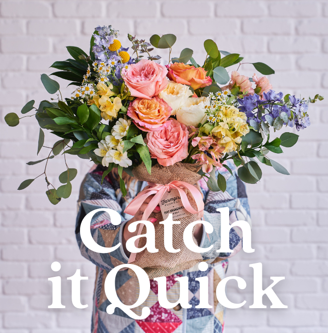 Catch it Quick. A pastel hand-tied bouquet in burlap wrap, held against a white brick wall.