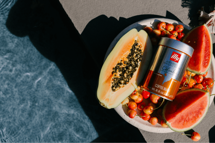 Halved papaya, watermelon slices, cherries, and a tin of illy coffee beans arranged on a plate by the pool