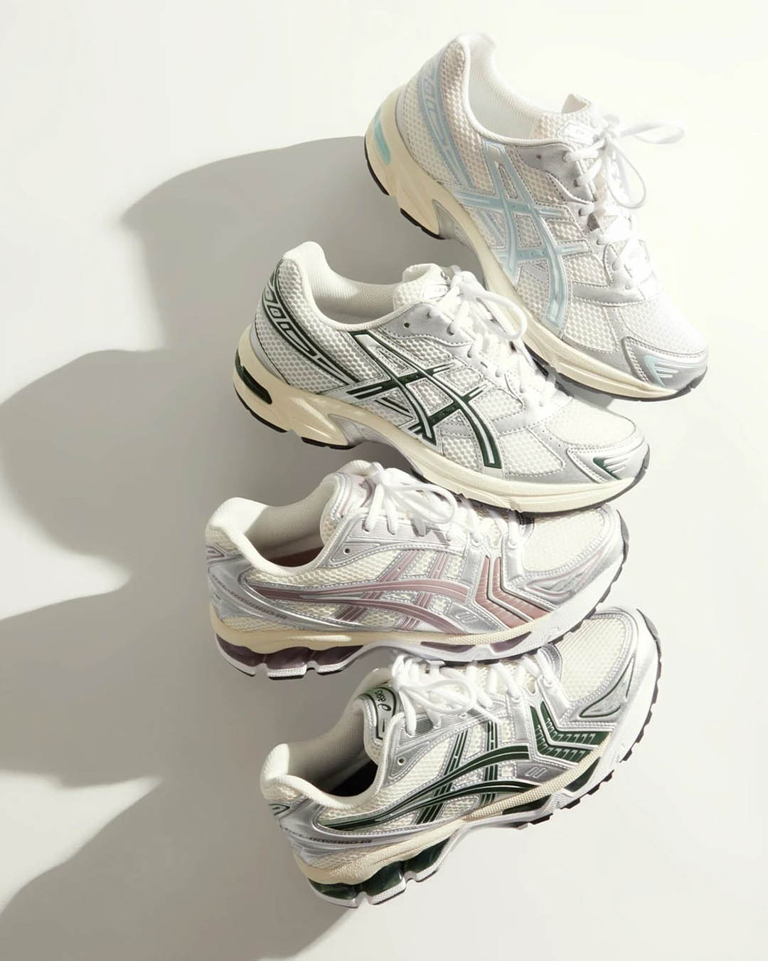 Four pairs of white mesh running trainers with green, blue and pink accents arranged diagonally on a pale background