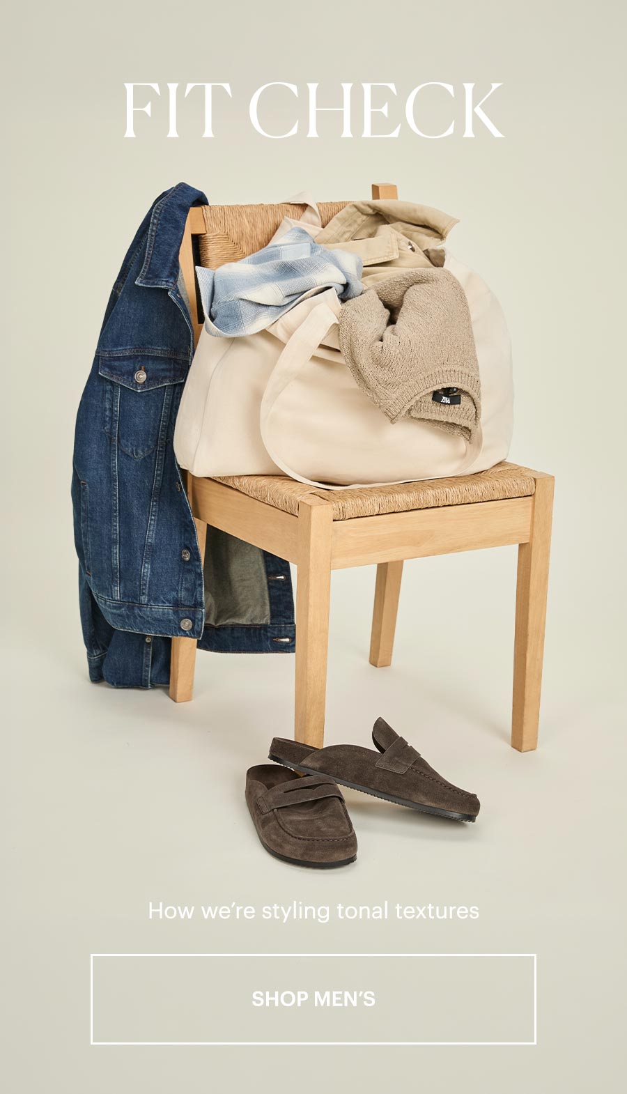 Fit Check - How we’re styling tonal textures. Featuring a tote bag of PAIGE men's items sitting on a light wooden chair, a dark wash denim jacket draped over the back and a pair of dark brown shearling slides resting in front. Shop Men's.