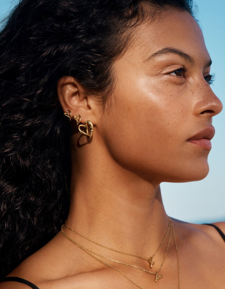 A model stares ahead in 14k gold-plated heart-shaped Pandora earrings.
