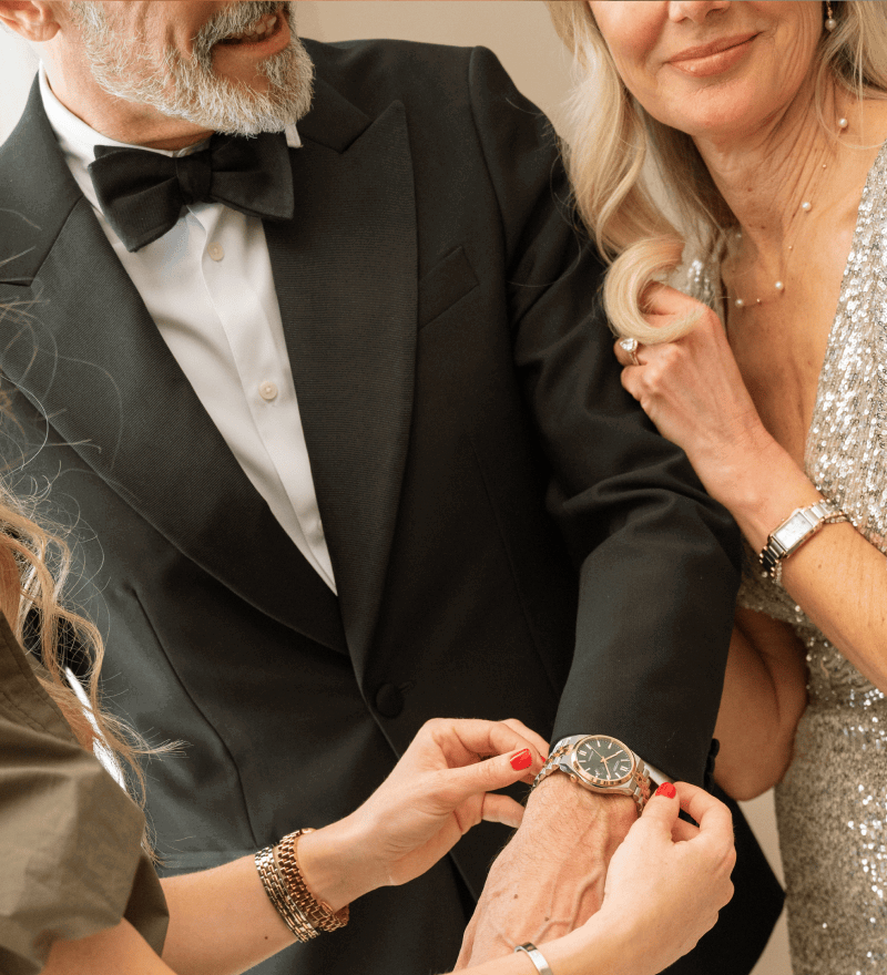 Man and woman dressed up for an event, wearing a variety of jewellery, including watches, necklaces and rings.