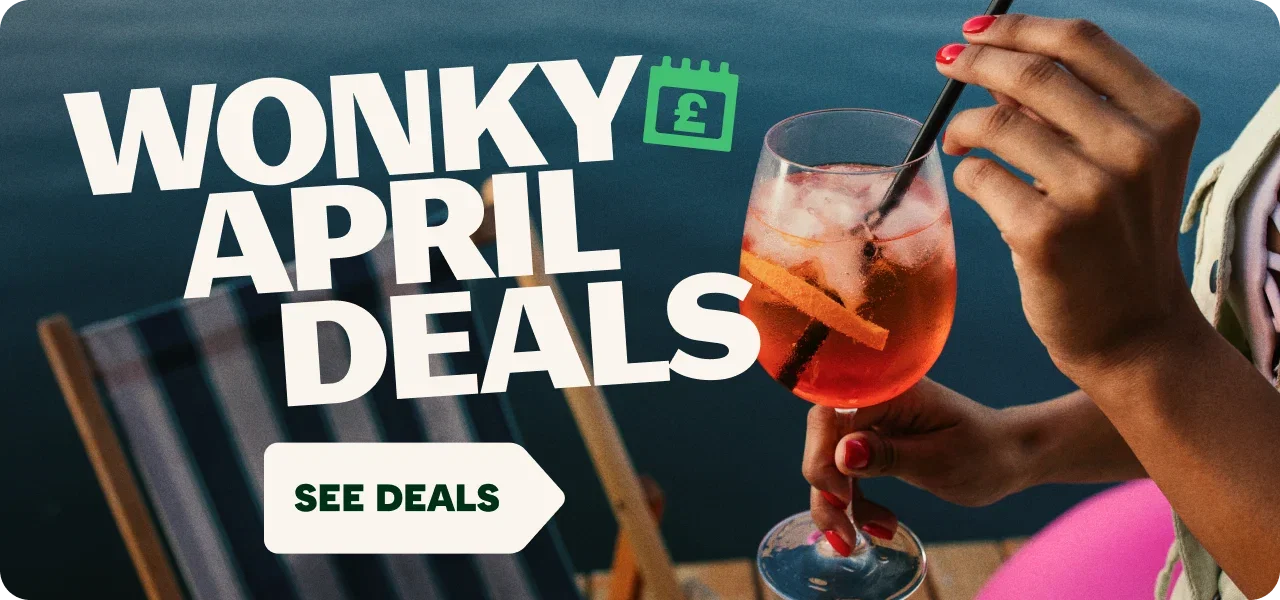 Promotional graphic advertising 'Wonky April Deals' Large white text reads 'WONKY APRIL DEALS' alongside a green calendar icon with a pound symbol. In the background, a person holds and stirs a red-orange iced drink in a wine glass near a waterfront setting. A white arrow-shaped button at the bottom reads 'SEE DEALS'.