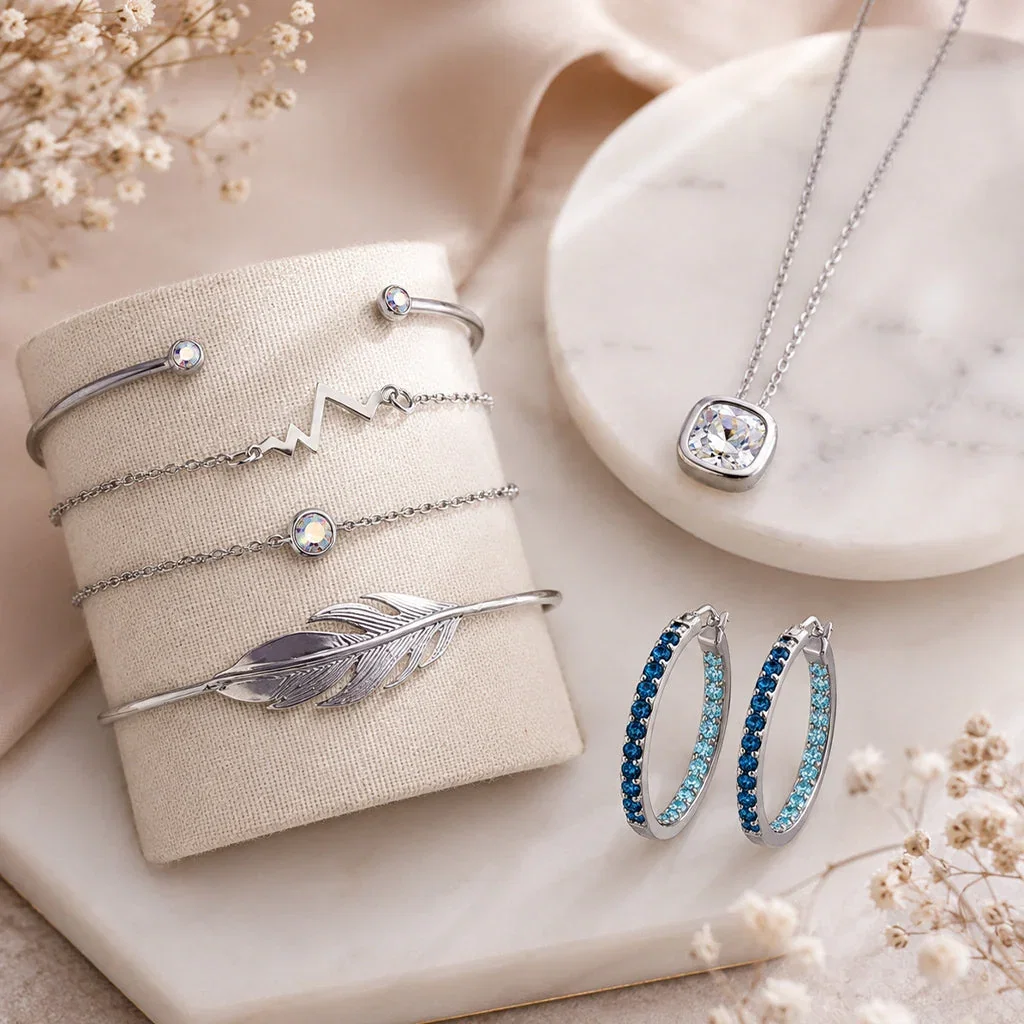 Silver jewelry collection featuring bracelets, necklaces, and earrings with crystals and gemstones displayed on marble surfaces.