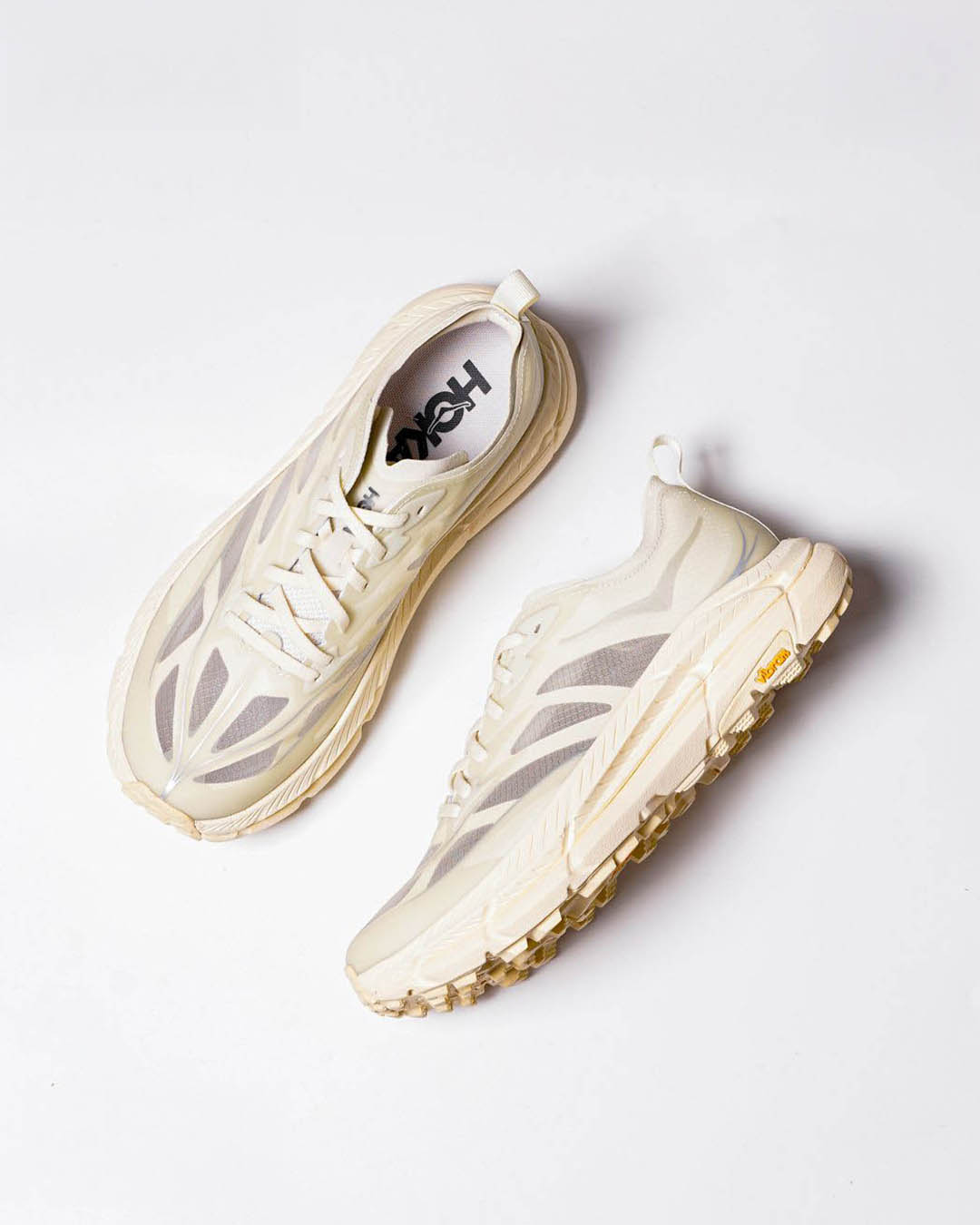 Pair of cream Hoka running shoes with chunky soles, top-down view on white background