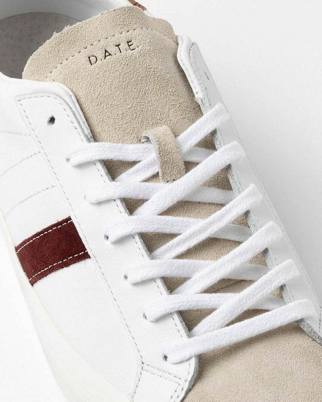 Close-up of white leather trainer with beige suede tongue, white laces and burgundy side stripe, top-down detail shot