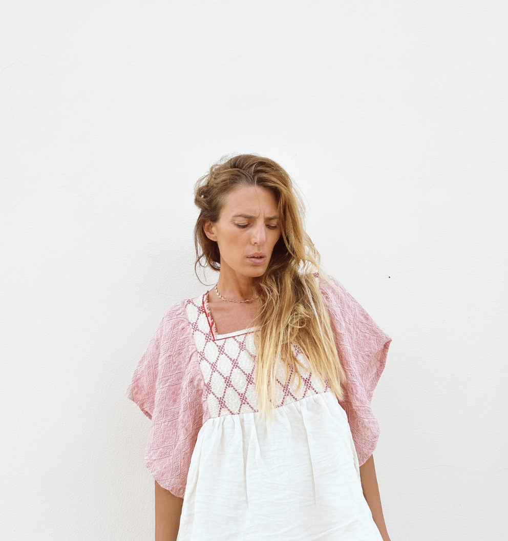 Woman in a white and pink embroidered dress looks down with her eyes closed.