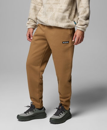Waist-down image of a man wearing brown sweats against a grey background.
