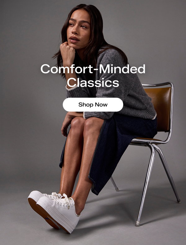 A woman leaning forward in a brown chair. She is wearing a grey sweater, denim high-slit skirt, and the Triple Up Leather Lace-Up in white. The email says Comfort-Minded Classics. Shop Now
