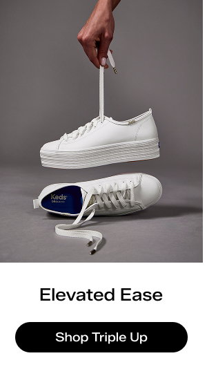 A grey background with the Triple Up Leather Lace-Ups in white, one on its side and one held up by its lace.  Elevated Ease Shop the Triple Up