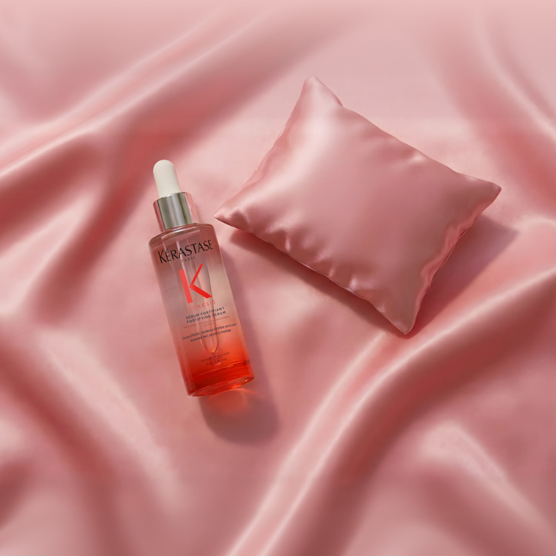  Siero Kérastase Genesis adagiato su seta rosa accanto a un cuscino decorativo