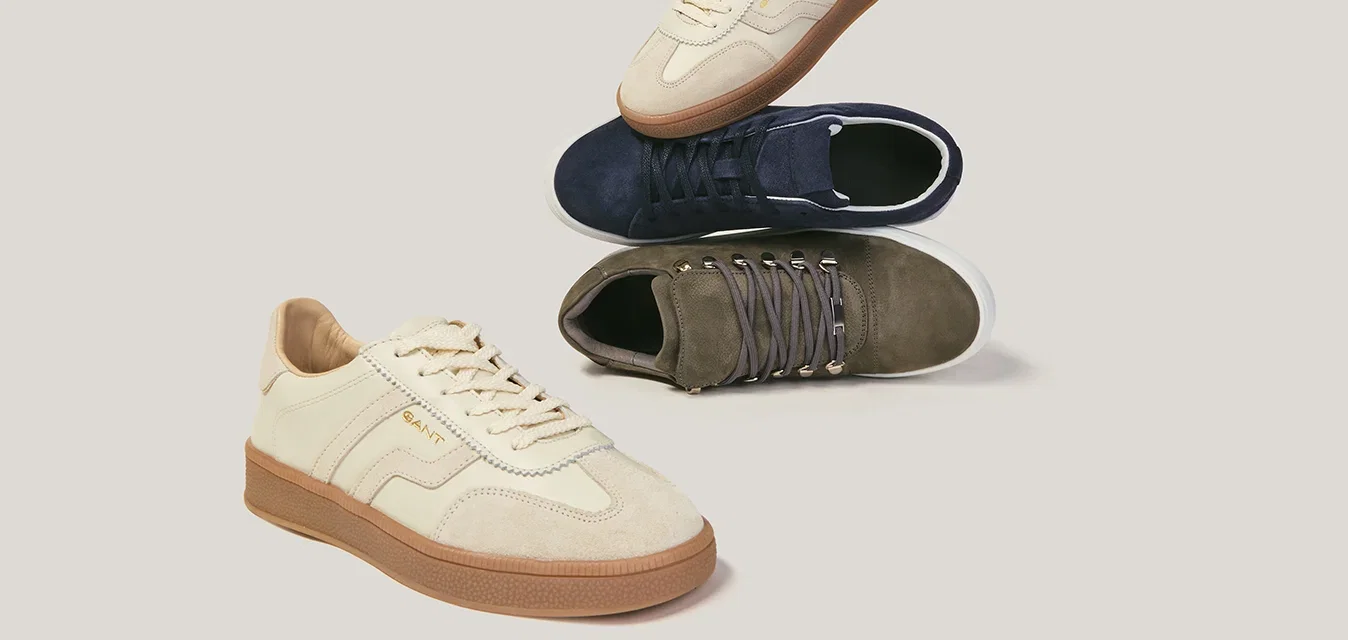 Tres pares de zapatillas casuales en beige, azul marino y verde oliva dispuestos sobre un fondo claro.