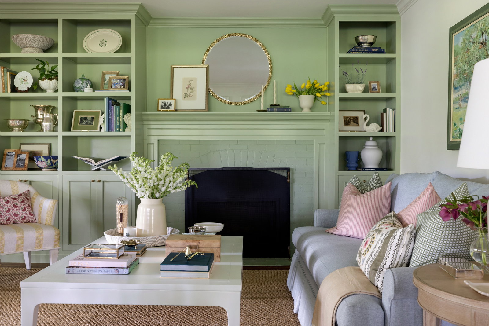 Living room with green painted fireplace and built in filled with accessories. A blue couch with a white coffee table in front styled with Brooke & Lou accessories.