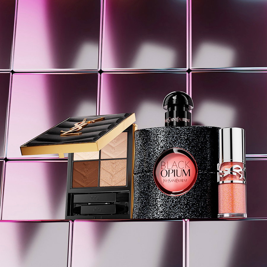 An eyeshadow palette, a glittery Black Opium perfume bottle, and a liquid gloss arranged on a shiny metallic tile background.