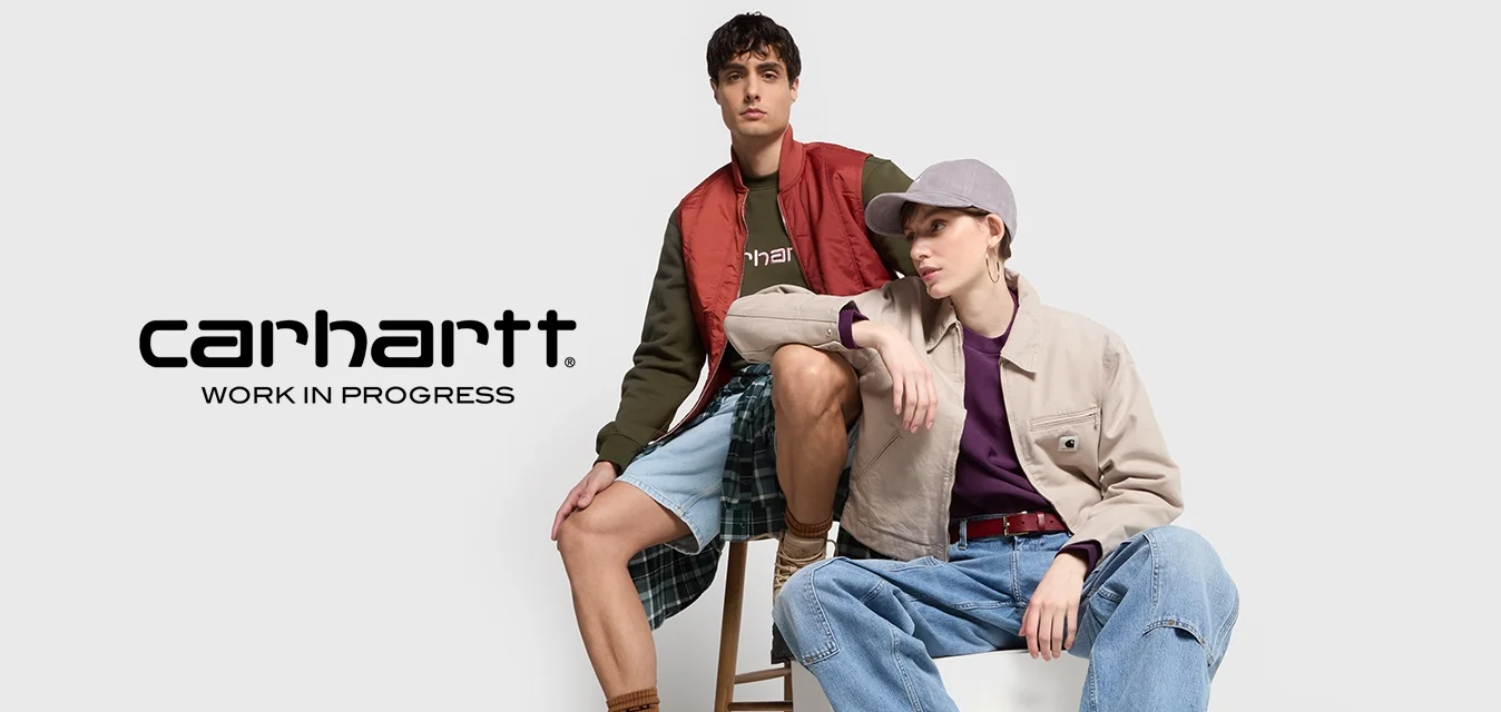 Dos modelos lucen atuendos casuales en capas. Uno lleva un chaleco acolchado rojo con una sudadera verde oscura, y el otro viste una chaqueta beige sobre una blusa marrón.