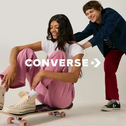 Jonge vrouw in roze broek zittend op een skateboard terwijl een glimlachende man haar van achteren duwt in een witte studio.