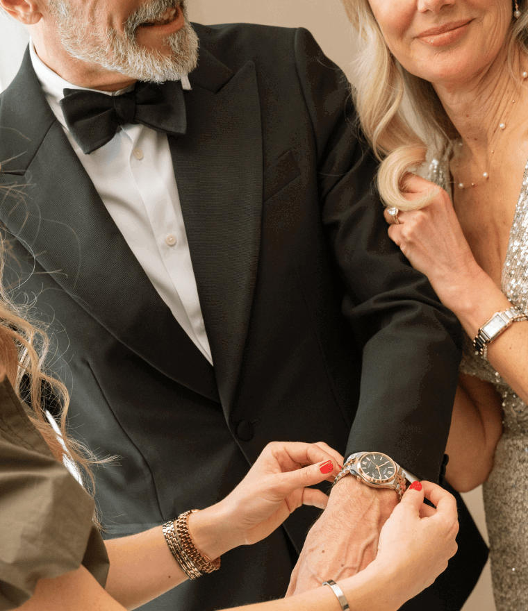 Man and woman dressed up for an event, wearing a variety of jewellery, including watches, necklaces and rings.