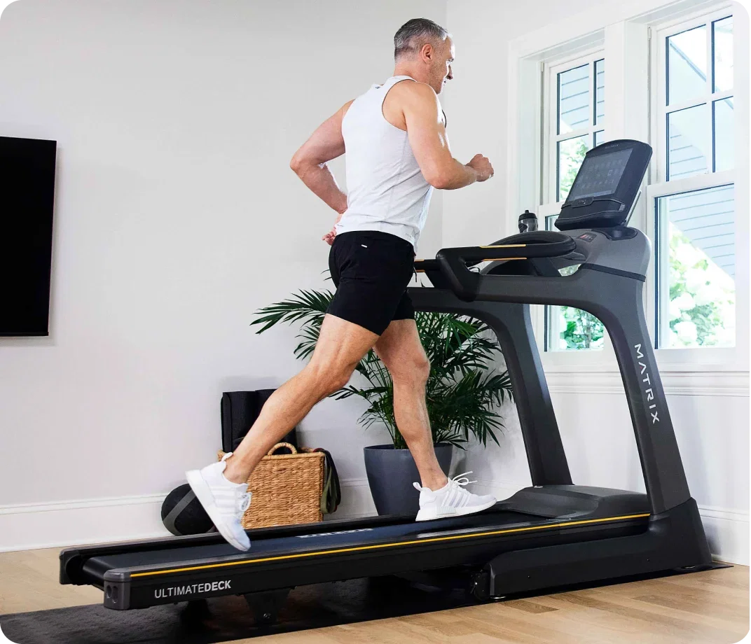 Man running on a Matrix treadmill in a bright home gym.