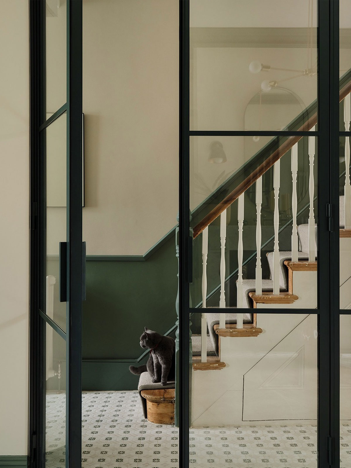 Elegant hallway with green panelling, glass doors, and a grey cat sitting on a stool.