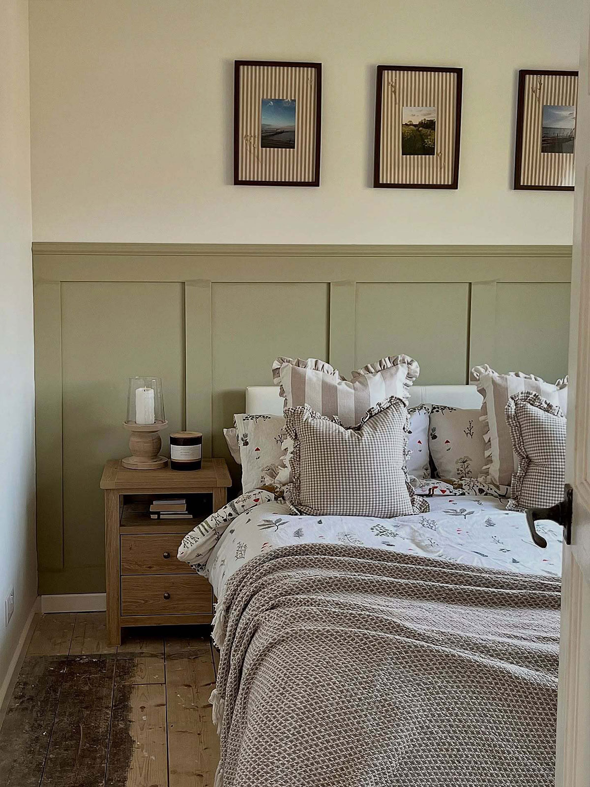 Calm bedroom with olive-green wall panelling, floral bedding, and framed photos above.