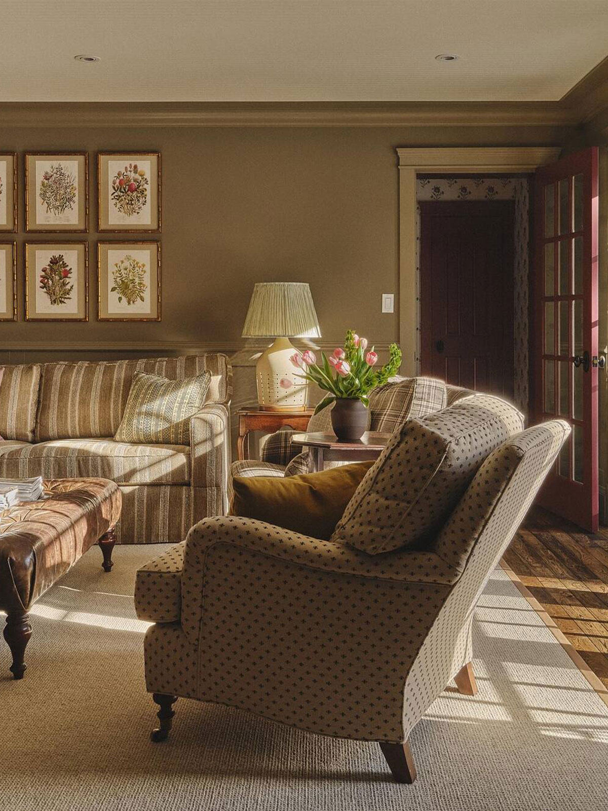 Warm, traditional living room with striped sofa, patterned armchairs, and framed botanical prints.