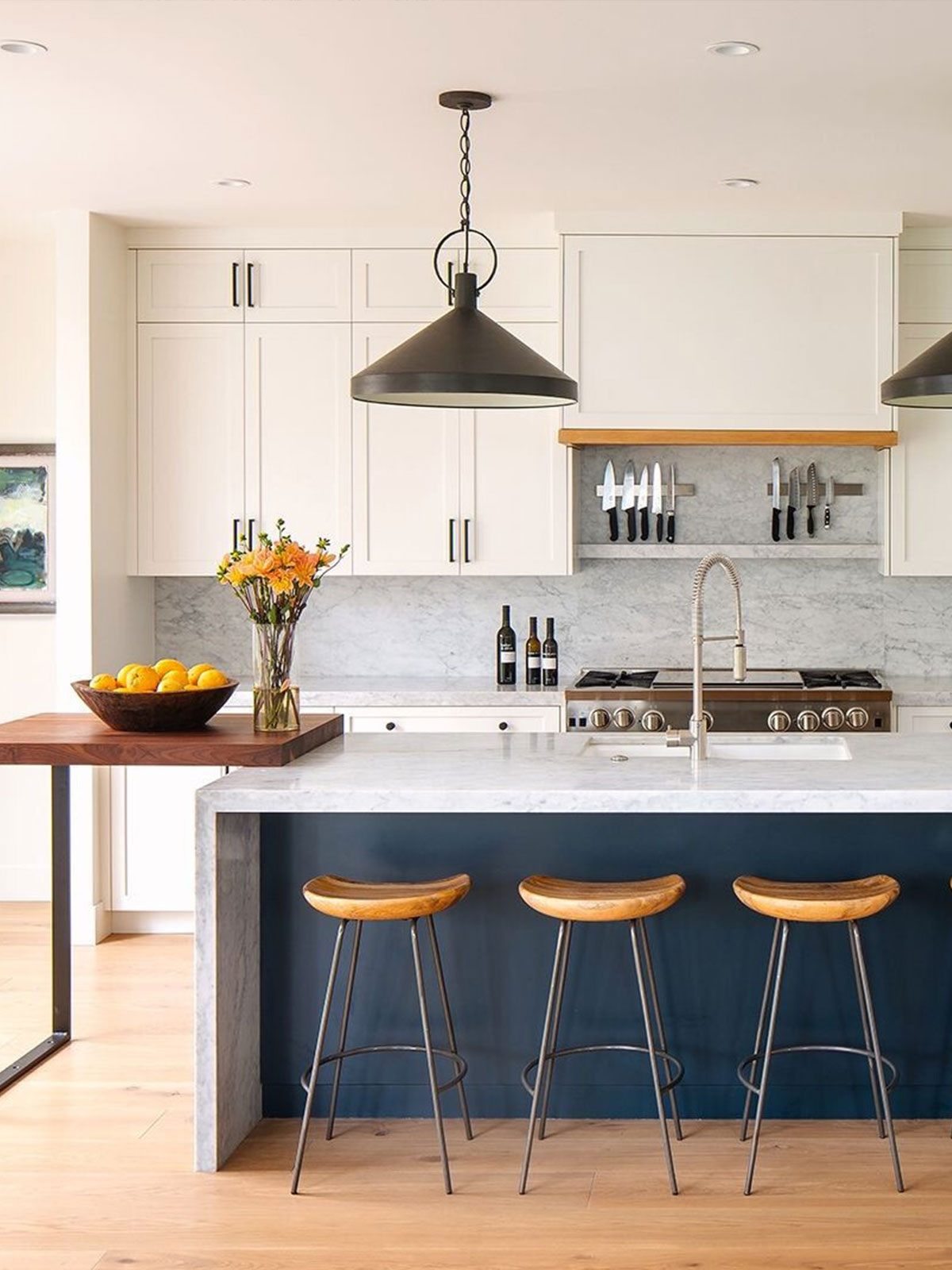 Bright kitchen with marble island, wooden stools, and white cabinets.
