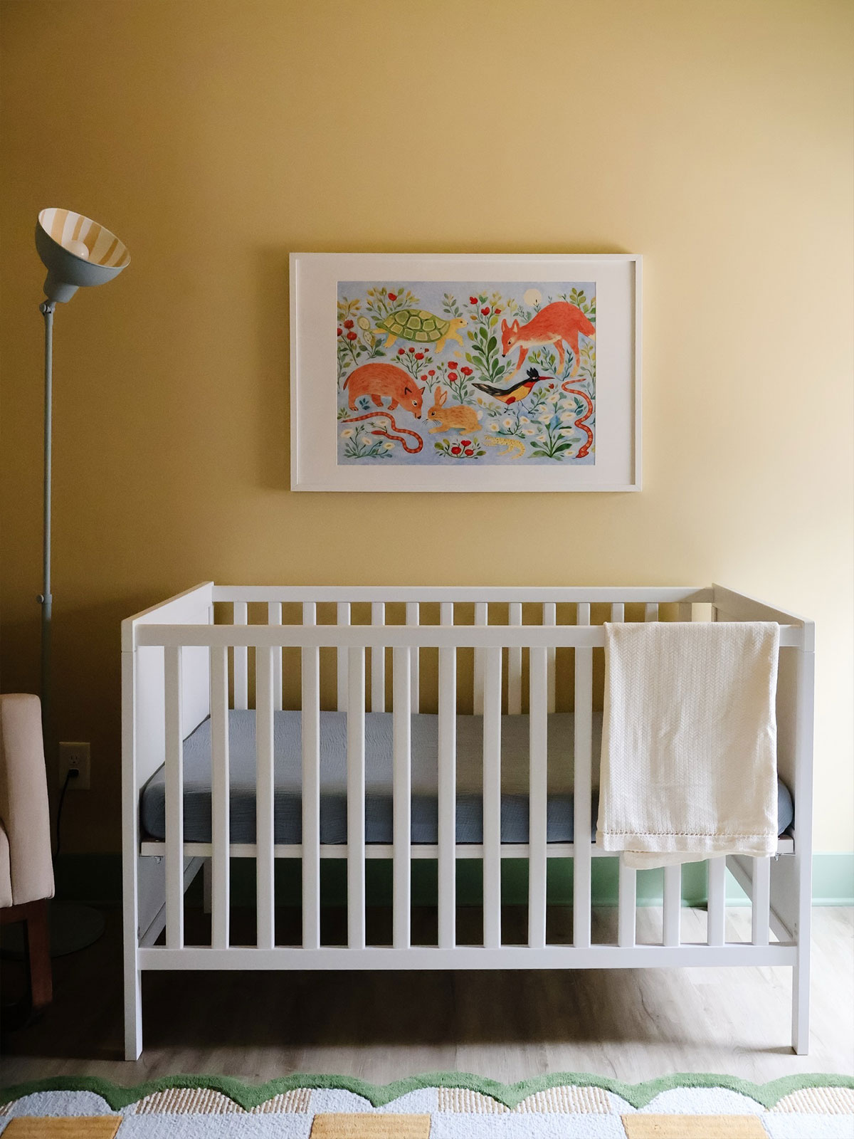 White cot against soft yellow wall with colourful animal artwork above.