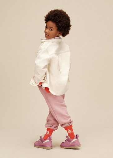A model in a studio wearing a white jacket, pink trousers and UGG trainers.