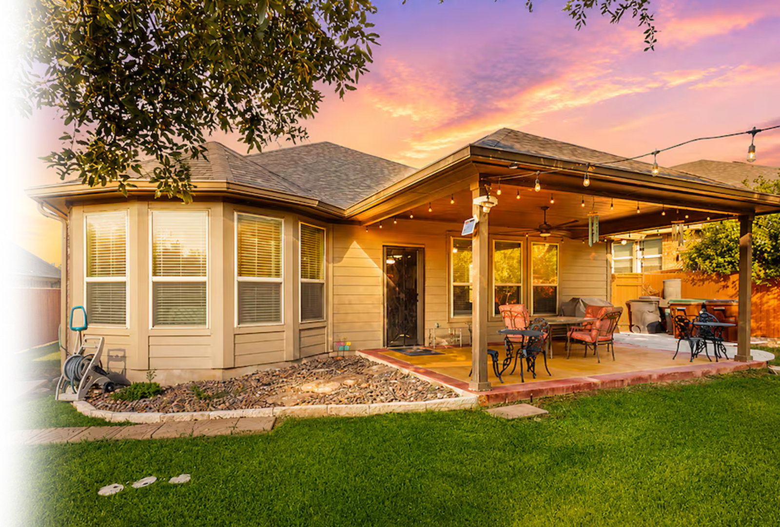 Beige house with covered patio, string lights, and vivid sunset sky.