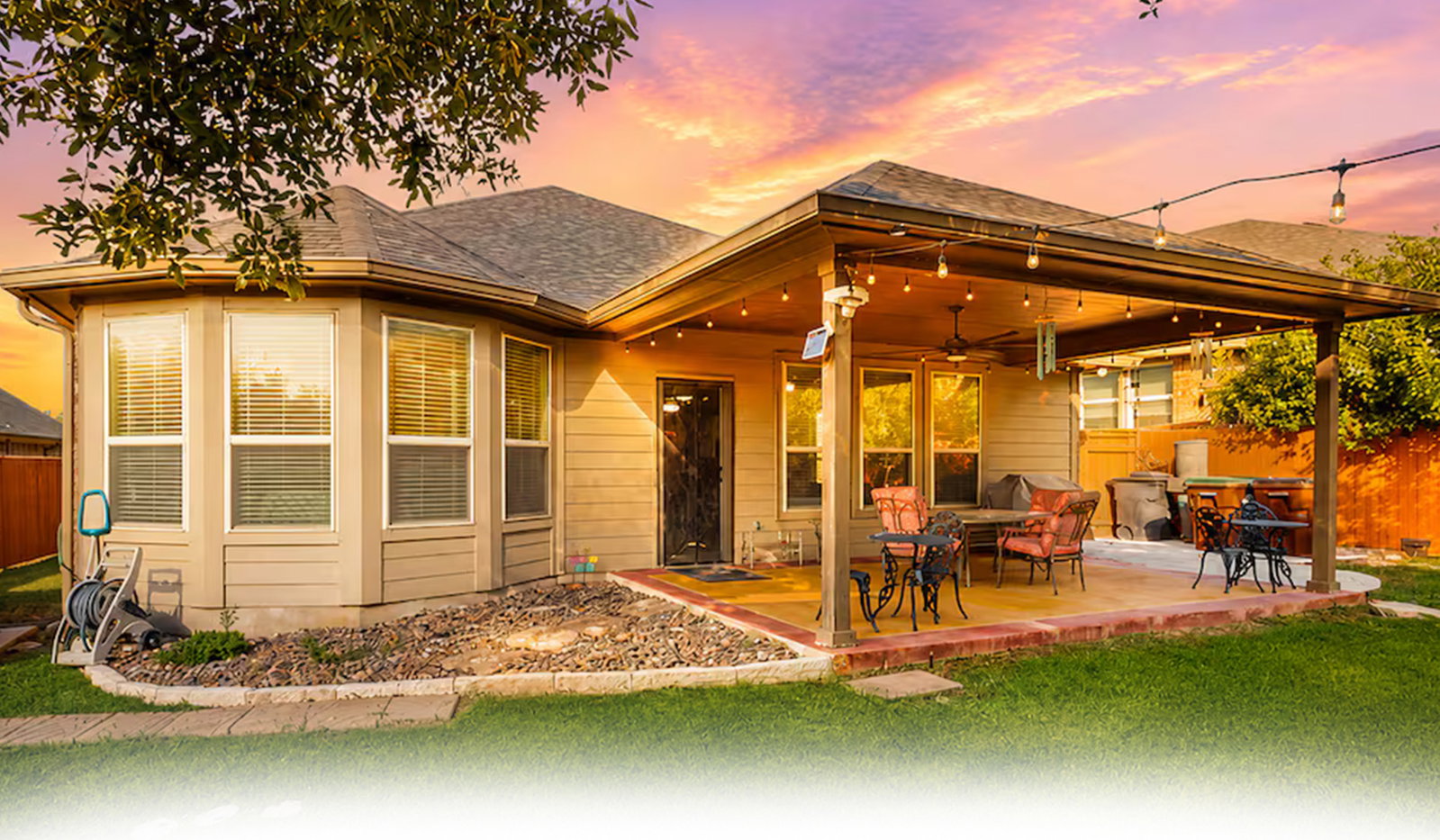 Beige house with covered patio, string lights, and vivid sunset sky.