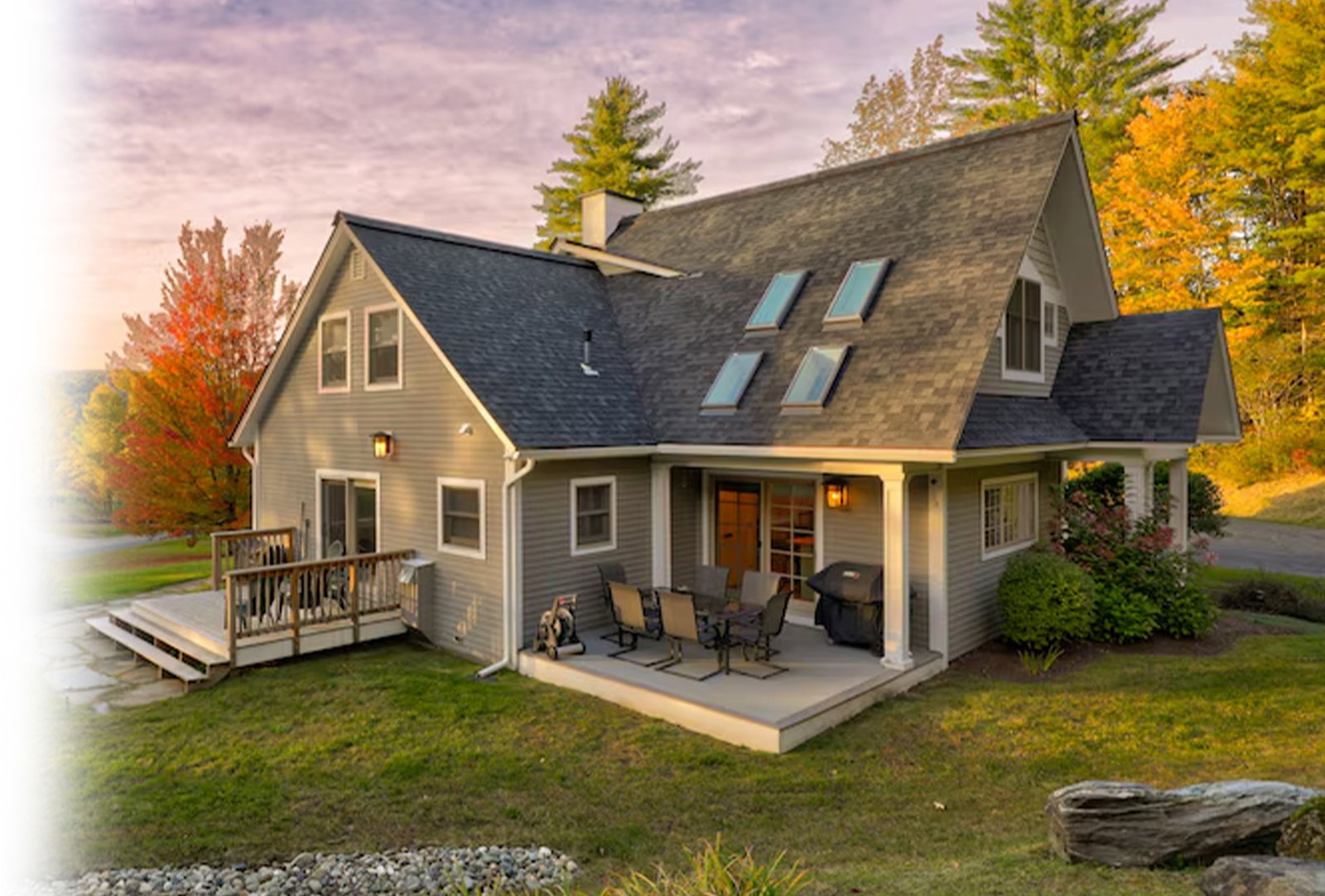 Gray contemporary farmhouse with skylights, porch, and autumn trees at sunset.