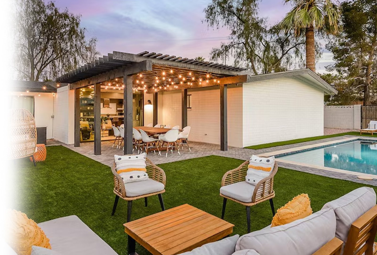 Modern backyard patio with outdoor dining area beneath a string-lit pergola and poolside lounge seating.