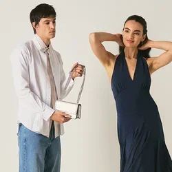 Uomo con camicia bianca e jeans che tiene una piccola borsa a mano accanto a una donna in abito blu navy che posa con le mani dietro la testa.