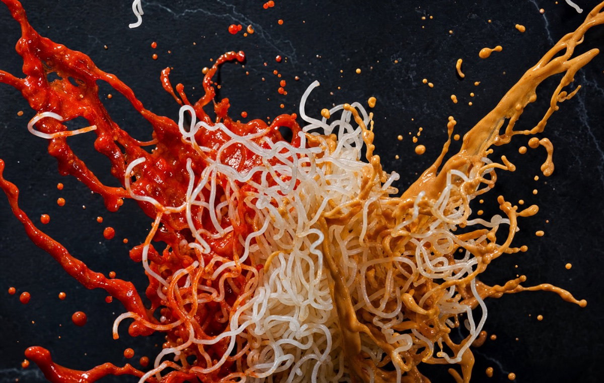 White konjac noodles caught mid-air between a marinara and a peanut sauce