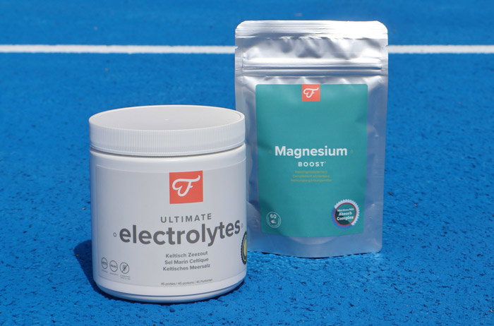White tub of 'Ultimate Electrolytes' and silver pouch of 'Magnesium Boost' supplements on a blue athletics track
